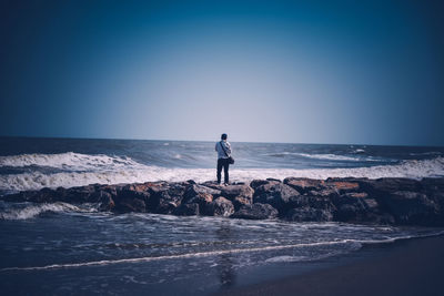 Man standing on rock by sea against clear sky