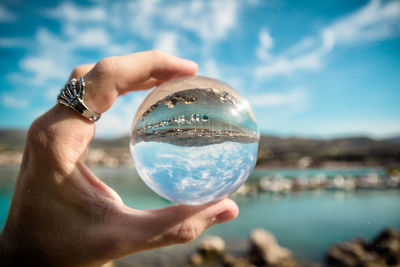 Close-up of hand holding crystal ball against sky