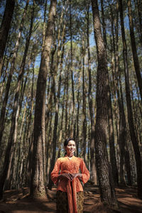Low angle view of woman standing by tree trunk in forest