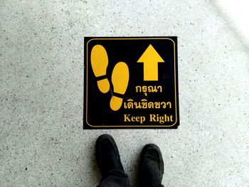 Low section of man standing by information sign with text on floor