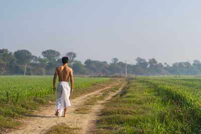 Rear view of man walking on field against clear sky