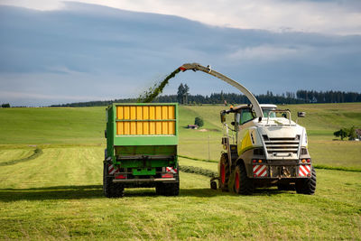 The combine pours silage into the tractor-trailer in the field. 