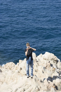 Young man photographing while standing on rock formation against sea