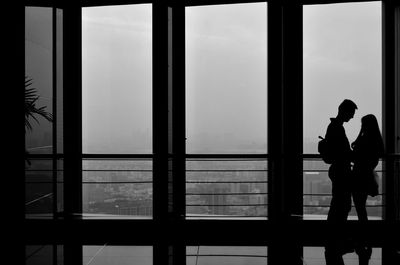 Silhouette man standing by window against sky