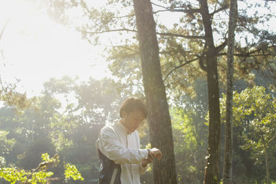 Side view of young man standing against trees in forest