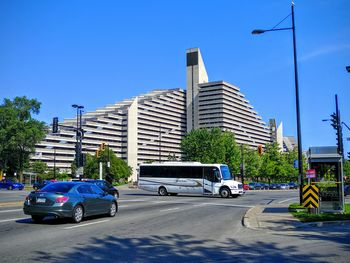 Cars on road by buildings against clear blue sky