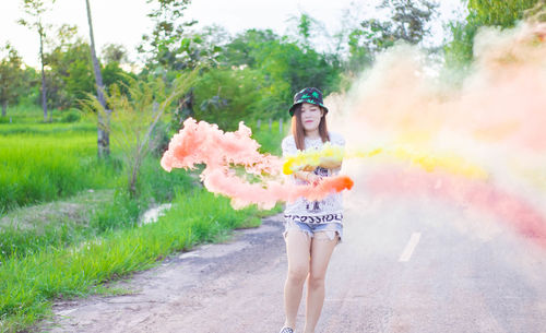Young woman holding distress flare emitting smokes on road