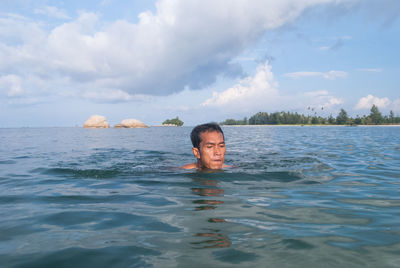 Man swimming in sea against cloudy sky