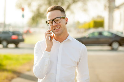 Smiling young man talking on mobile phone while standing in city