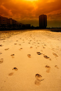 Footprints on sand at beach against sky during sunset