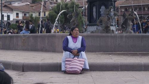 Full length of woman sitting on street against buildings in city