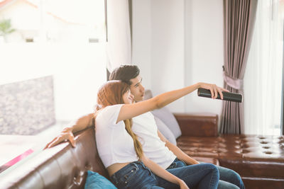 Young couple watching tv while sitting on sofa at home