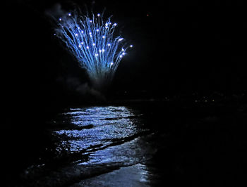 Firework display over sea against sky at night