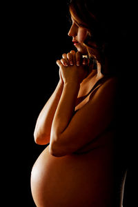 Portrait of naked pregnant woman praying against black background