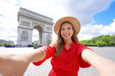 Happy young traveler woman taking selfie photo with arc de triomphe in paris, france