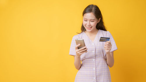 Portrait of a smiling young woman holding drink against yellow background