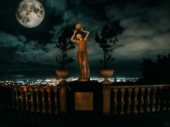 Statue against illuminated trees at night