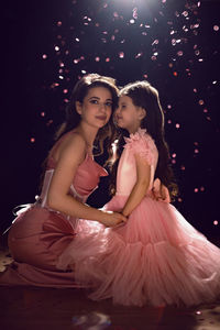 Mom and daughter in pink dresses sitting on the floor at christmas at night with a lamp 