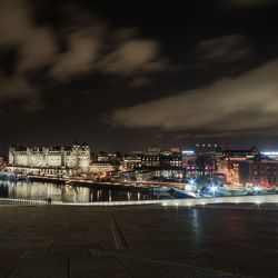 Illuminated buildings by river against sky in city at night