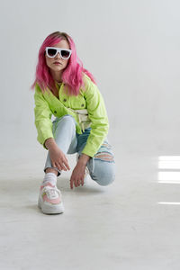 Portrait of young woman wearing sunglasses while standing against wall