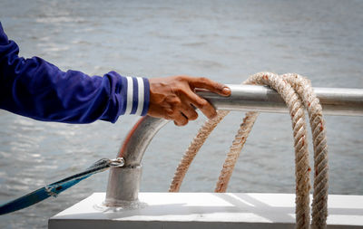 Cropped hand of man by rope against sea