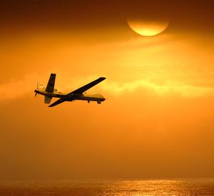 Airplane flying over sea against sky during sunset