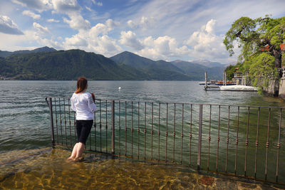 Rear view of woman standing by sea against sky