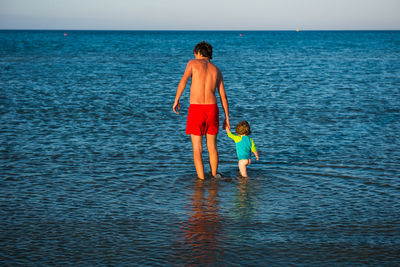 Rear view of siblings standing on beach