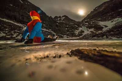 Person sitting on frozen lake against snowcapped mountains