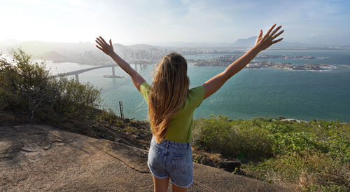 Successful woman with hands raised up on mountain peak enjoying scenery at sunset