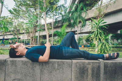 Side view of man lying down on wall against trees