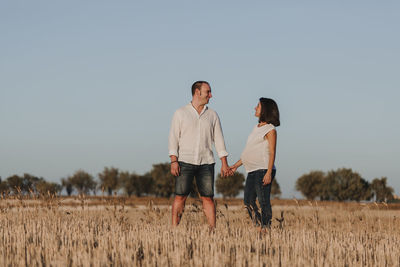 Smiling man holding hands of pregnant girlfriend while standing on field