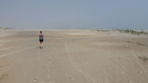 Rear view of woman walking on beach against foggy sky