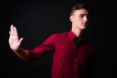 Portrait of young man looking away against black background