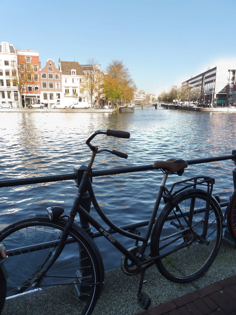 BICYCLE ON RAILING BY RIVER AGAINST BUILDINGS