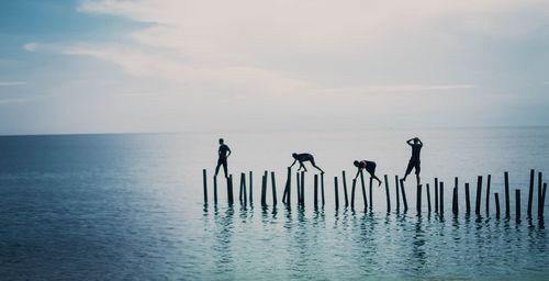 Friends walking on wooden posts in sea
