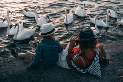 High angle view of woman with son sitting by swan swimming in lake