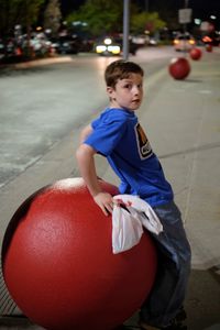 Portrait of boy standing against large ball in city