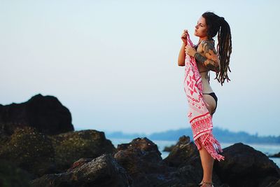 Woman standing on rock by sea against sky