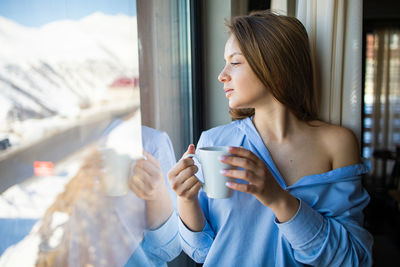 Beautiful woman with tea cup looking at window in morning