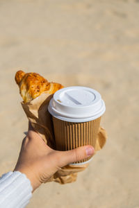 Cropped hand of woman holding coffee at beach