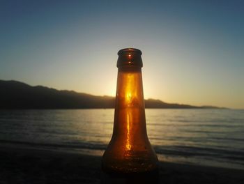 Close-up of bottle on beach against sky during sunset