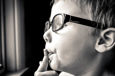 Close-up of boy wearing eyeglasses while looking through window at home