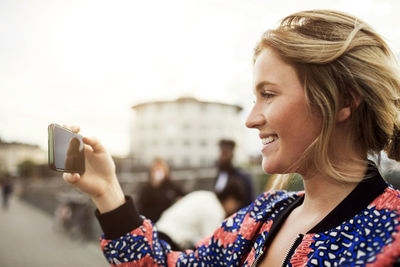 Side view of happy woman photographing from smart phone