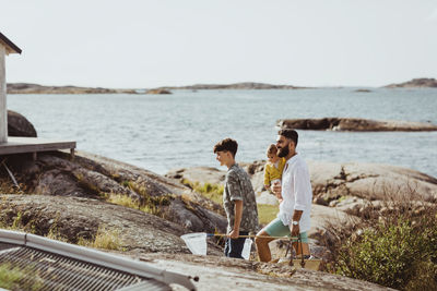 Side view of father with children walking on rock formation during sunny day