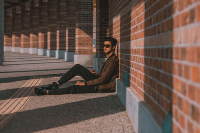 Young man sitting against brick wall