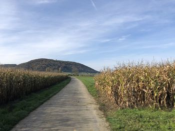 Dirt road amidst field against sky