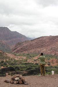 Rear view of man standing on mountain against sky