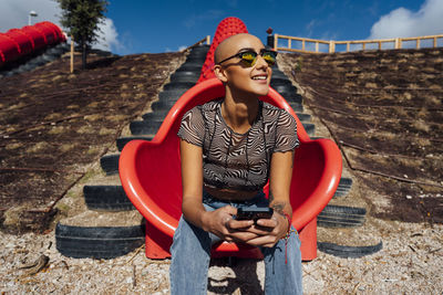 Smiling young woman wearing sunglasses holding smart phone at park