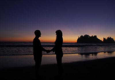 Silhouette couple standing at beach during sunset